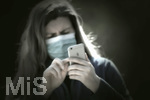 08.04.2020, Symbolbild, Corona-Krise, Frau schaut auf ihr Handy mit  Gesichtsmaske.