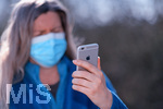 08.04.2020, Symbolbild, Corona-Krise, Frau schaut auf ihr Handy mit Gummihandschuhe und Gesichtsmaske.