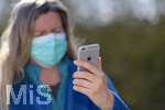 08.04.2020, Symbolbild, Corona-Krise, Frau schaut auf ihr Handy mit Gummihandschuhe und Gesichtsmaske.
