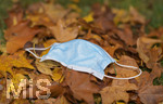 19.10.2020, Symbolbild, Corona-Krise, Eine Einweg-Maske liegt auf einem Bltterhaufen unter einem Baum mit Herbstlaub.