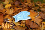 19.10.2020, Symbolbild, Corona-Krise, Eine Einweg-Maske liegt auf einem Bltterhaufen unter einem Baum mit Herbstlaub.