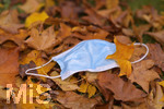 19.10.2020, Symbolbild, Corona-Krise, Eine Einweg-Maske liegt auf einem Bltterhaufen unter einem Baum mit Herbstlaub.