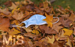19.10.2020, Symbolbild, Corona-Krise, Eine Einweg-Maske liegt auf einem Bltterhaufen unter einem Baum mit Herbstlaub.