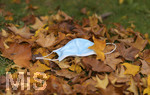 19.10.2020, Symbolbild, Corona-Krise, Eine Einweg-Maske liegt auf einem Bltterhaufen unter einem Baum mit Herbstlaub.