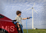 16.08.2021, Symbolbild Ökostrom für E-Autos. Ein roter Tesla lädt symbolisch direkt an der Windkraftanlage im Allgäu. (Model Release vorhanden) 