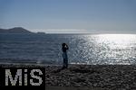 02.09.2023, Irland Land und Leute, Roadtrip am Ring of Kerry, der Kstenstrasse am Atlantik entlang im County Kerry.   Waterville Beach, Junge Frau fotografiert am Meer mit ihrem Handy in die Sonne.