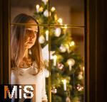 15.11.2023, Weihnachten 2023 in Deutschland, Ein festlich dekorierter Weihnachtsbaum in einer Wohnung im Unterallgu.  Eine Frau schaut nachdenklich aus dem Wohnzimmer durchs Fenster, sie ist alleine. Thema: Angst vor Einsamkeit am Heiligen Abend. (Modelreleased)