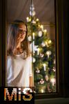 15.11.2023, Weihnachten 2023 in Deutschland, Ein festlich dekorierter Weihnachtsbaum in einer Wohnung im Unterallgu.  Eine Frau schaut nachdenklich aus dem Wohnzimmer durchs Fenster, sie ist alleine. Thema: Angst vor Einsamkeit am Heiligen Abend. (Modelreleased)
