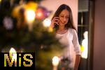 15.11.2023, Weihnachten 2023 in Deutschland, Ein festlich dekorierter Weihnachtsbaum in einer Wohnung im Unterallgäu.  Eine Frau telefoniert im Wohnzimmer mit ihren Freunden oder Familie am Heiligen Abend. (Modelreleased) 