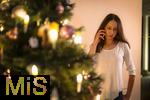 15.11.2023, Weihnachten 2023 in Deutschland, Ein festlich dekorierter Weihnachtsbaum in einer Wohnung im Unterallgäu.  Eine Frau telefoniert im Wohnzimmer mit ihren Freunden oder Familie am Heiligen Abend. (Modelreleased) 