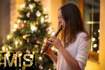 15.11.2023, Weihnachten 2023 in Deutschland, Ein festlich dekorierter Weihnachtsbaum in einer Wohnung im Unterallgäu.  Eine Frau spielt Blockflöte im Wohnzimmer am Heiligen Abend. (Modelreleased) 