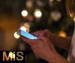 15.11.2023, Weihnachten 2023 in Deutschland, Ein festlich dekorierter Weihnachtsbaum in einer Wohnung im Unterallgu. Eine Frau schreibt eine Weihnachts-Nachricht auf ihrem Handy.
