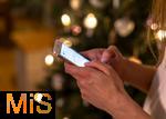 15.11.2023, Weihnachten 2023 in Deutschland, Ein festlich dekorierter Weihnachtsbaum in einer Wohnung im Unterallgäu. Eine Frau schreibt eine Weihnachts-Nachricht auf ihrem Handy.
