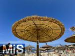 23.06.2025,  Beliebtes Reiseziel der Deutschen, Mallorca.  hier Cala Ratjada am Strand Cala Agulla. Traditionelle Stroh-Sonnenschirme unter blauem Himmel.