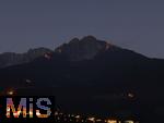 29.6.2025, Meran in Sdtirol, Italien. Herz-Jesu-Feuer auf dem Gebirgsgrat des Ifinger Berggipfel.
Der Brauch, im Juni Feuer zu entznden, geht auf frhere Sonnwend- bzw. Johannisfeuer zurck, welche in Erinnerung an das Herz-Jesu-Gelbnis von 1796 umgedeutet wurden. Unten leuchtet das Dorf Tirol in der Dmmerung.