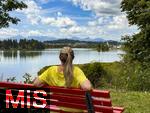 18.07.2025, Lechbruck am See im Allgu, Sommerurlaub in der Heimat. Frau rastet an einer Bank mit Blick auf den idyllischen Lech-Stausee