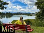 18.07.2025, Lechbruck am See im Allgu, Sommerurlaub in der Heimat. Frau rastet an einer Bank mit Blick auf den idyllischen Lech-Stausee