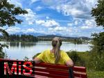 18.07.2025, Lechbruck am See im Allgu, Sommerurlaub in der Heimat. Frau rastet an einer Bank mit Blick auf den idyllischen Lech-Stausee