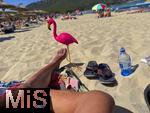 23.07.2025,  Beliebtes Reiseziel der Deutschen, Mallorca. Hier Cala Ratjada am Strand Cala Agulla. Eine pinke Flamingofigur steckt im Sand. Eine Urlaubergruppe aus Deutschland hat diese Spassfigur zum Scherz als Malle-Maskottchen mitgebracht. 