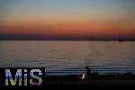 09.08.2025, Bregenz am Bodensee, Abendrot taucht den stillen See in mystisches Licht. Am Ufer hat jemand ein Lagerfeuer entzndet.