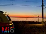 09.08.2025, Bregenz am Bodensee, Abendrot taucht den stillen See in mystisches Licht. Am Ufer hat jemand ein Lagerfeuer entzndet. Der Regionalexpress der Deutschen Bahn fhrt vorbei.