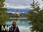 03.09.2025, Bled, Slowenien, Der Bleder See, auch Veldeser See oder Felder See, slowenisch Blejsko jezero, ist ein See in der slowenischen Region Oberkrain (Gorenjska) beim Kurort Bled. Blick  auf die Insel Blejski Otok mit der bekannten Marienkirche mitten im See. Besucherin steht am See.
