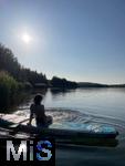 10.05.2025, Deutschland, Sachsen, Junge Frau sitzt an einem See auf einem SUP in der Sonne. (Modelreleased)