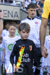 25.04.2026, Fussball 1. Bundesliga 2025/2026, 31.Spieltag, FC Augsburg - Eintracht Frankfurt, in der WWK-Arena Augsburg. Mannschaften und Schiedsrichter stehen zum Einlauf aufs Spielfeld bereit, sie kommen traditionell durch das schmiedeeisernem Eingangstor, das ein römisches Tor stilisieren soll, wegen der römischen Geschichte und Vergangeheit Augsburgs, Linienrichter Dominik Schaal kommt aufs Feld mit einem Kind der Einlaufeskorte mit der Linienrichter-Fahne