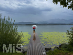 20.08.2026, am Hopfensee bei Füssen im Allgäu, Ein Steg führt in den See, hinten zieht ein Gewitter auf wo der Regen bereits aus den Wolken fällt. Eine Frau steht mit Regenschirm am Ende des Steges. (Modelreleased)