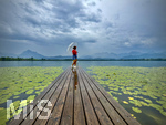 20.08.2026, am Hopfensee bei Füssen im Allgäu, Ein Steg führt in den See, hinten zieht ein Gewitter auf wo der Regen bereits aus den Wolken fällt. Eine Frau steht mit Regenschirm am Ende des Steges. (Modelreleased)