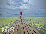 20.08.2026, am Hopfensee bei Füssen im Allgäu, Ein Steg führt in den See, hinten zieht ein Gewitter auf wo der Regen bereits aus den Wolken fällt. Eine Frau steht mit Regenschirm am Ende des Steges. (Modelreleased)