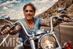 19.10.2026, (Landschaft KI-Generiert) Motorradfahrer mit Tattoos auf einem Highway in den USA, unterwegs auf einer Chopper. (Modelreleased)